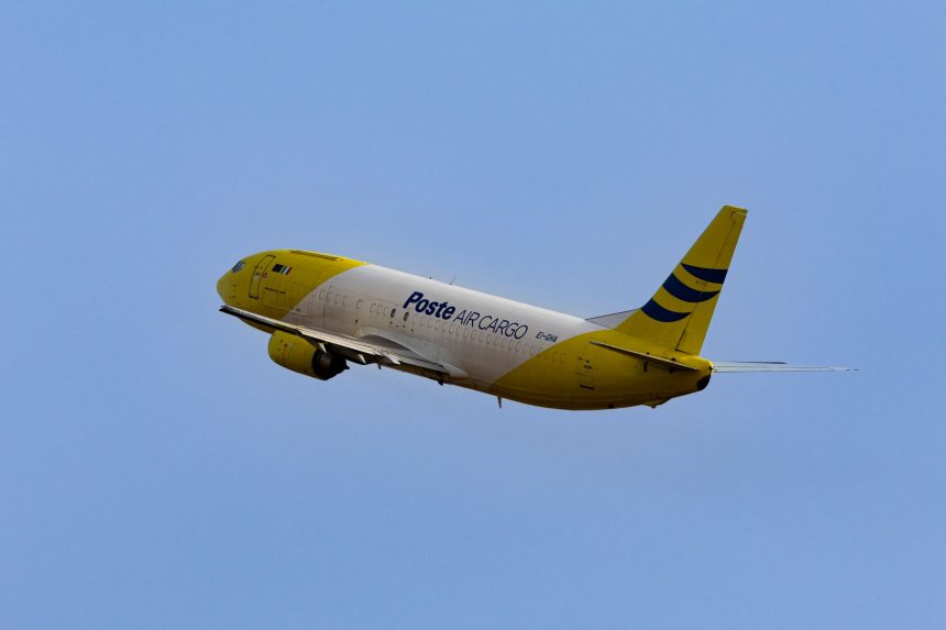 Aeronave cargueira amarela e branca decolando de um aeroporto sob céu claro.