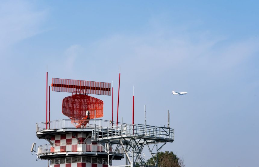 Torre de radar próxima a um avião contra o céu azul.