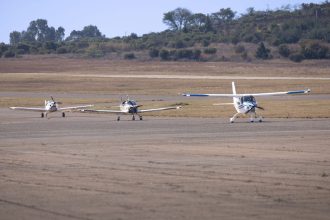 Três aeronaves ligeiras estacionadas numa pista rural sob céu azul.