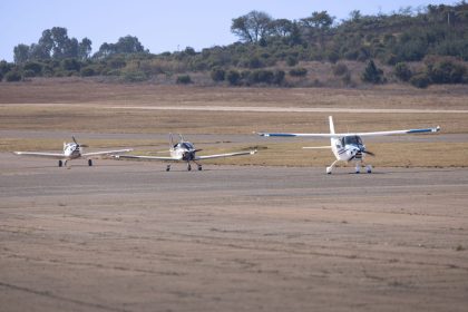 Três aeronaves ligeiras estacionadas numa pista rural sob céu azul.