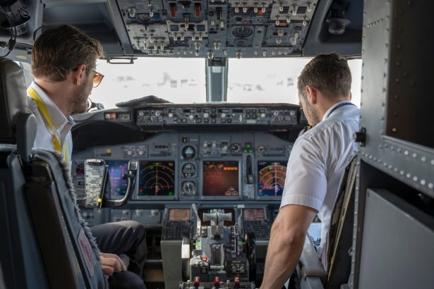 Dois pilotos operam os sistemas e instrumentos de um cockpit de avião comercial.