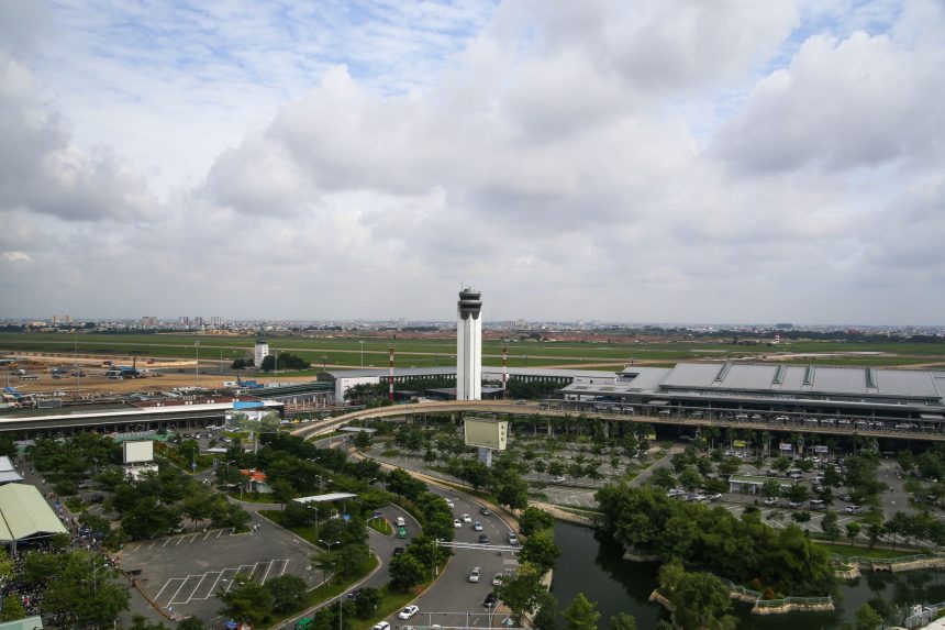 Vista aérea de um aeroporto movimentado, com torre de controle e áreas do entorno.
